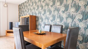 Comedor con mesa de madera, sillas negras, un armario y un papel tapiz estampado.