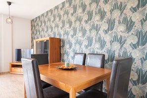 A dining area with a wooden table, black chairs, a cabinet, and a patterned wallpaper.