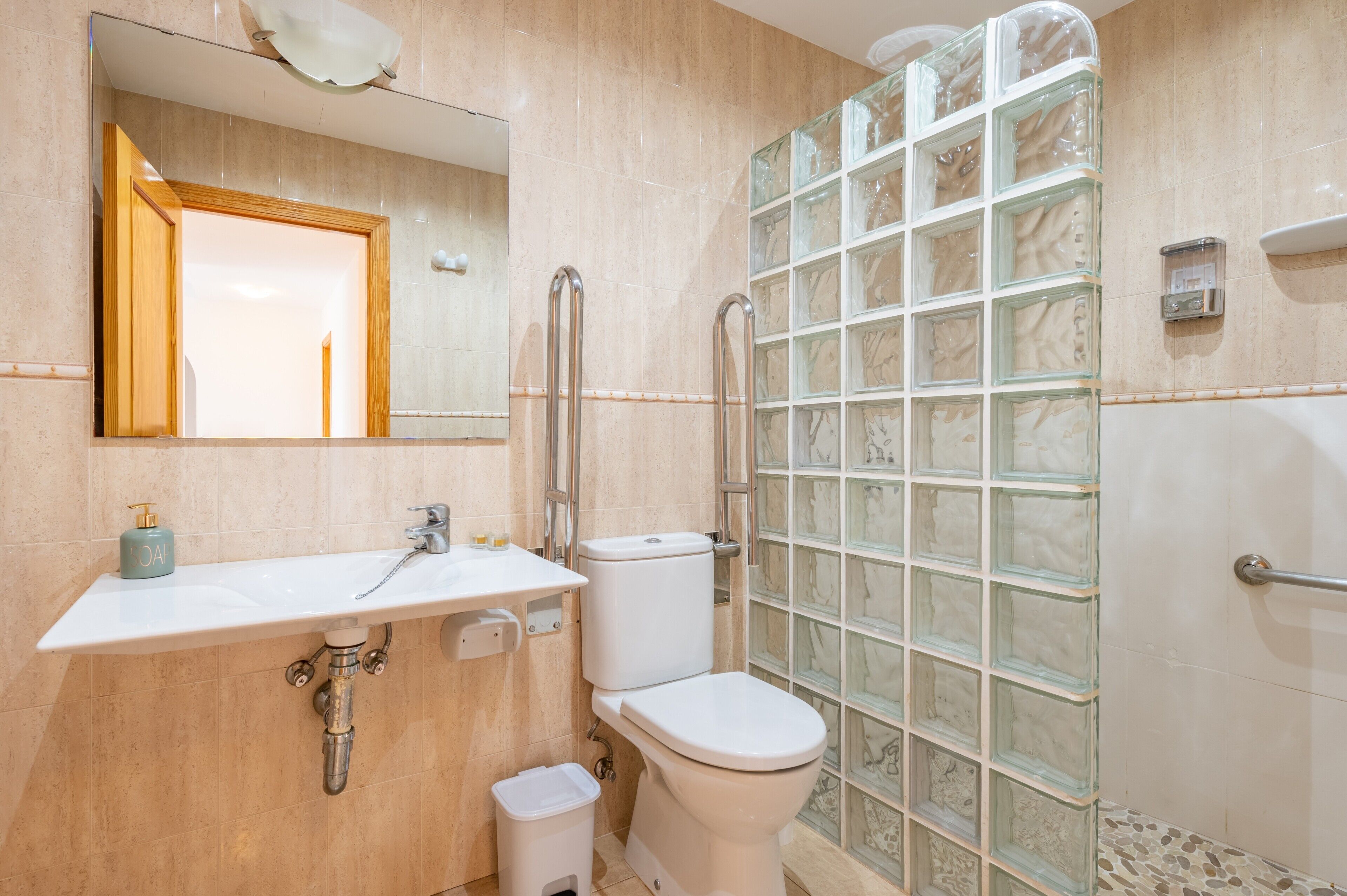 A bathroom with a white sink, mirror, toilet, and a glass shower enclosure.