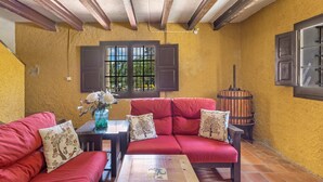A room with a red sofa, a wooden table, and a window with bars. - Country House 'Can Marc' with Mountain View, Private Pool and Wi-Fi (Dosrius)