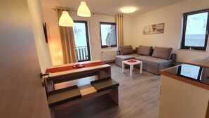 En kompakt opholdsstue med sofa, spisebord og tekøkken.