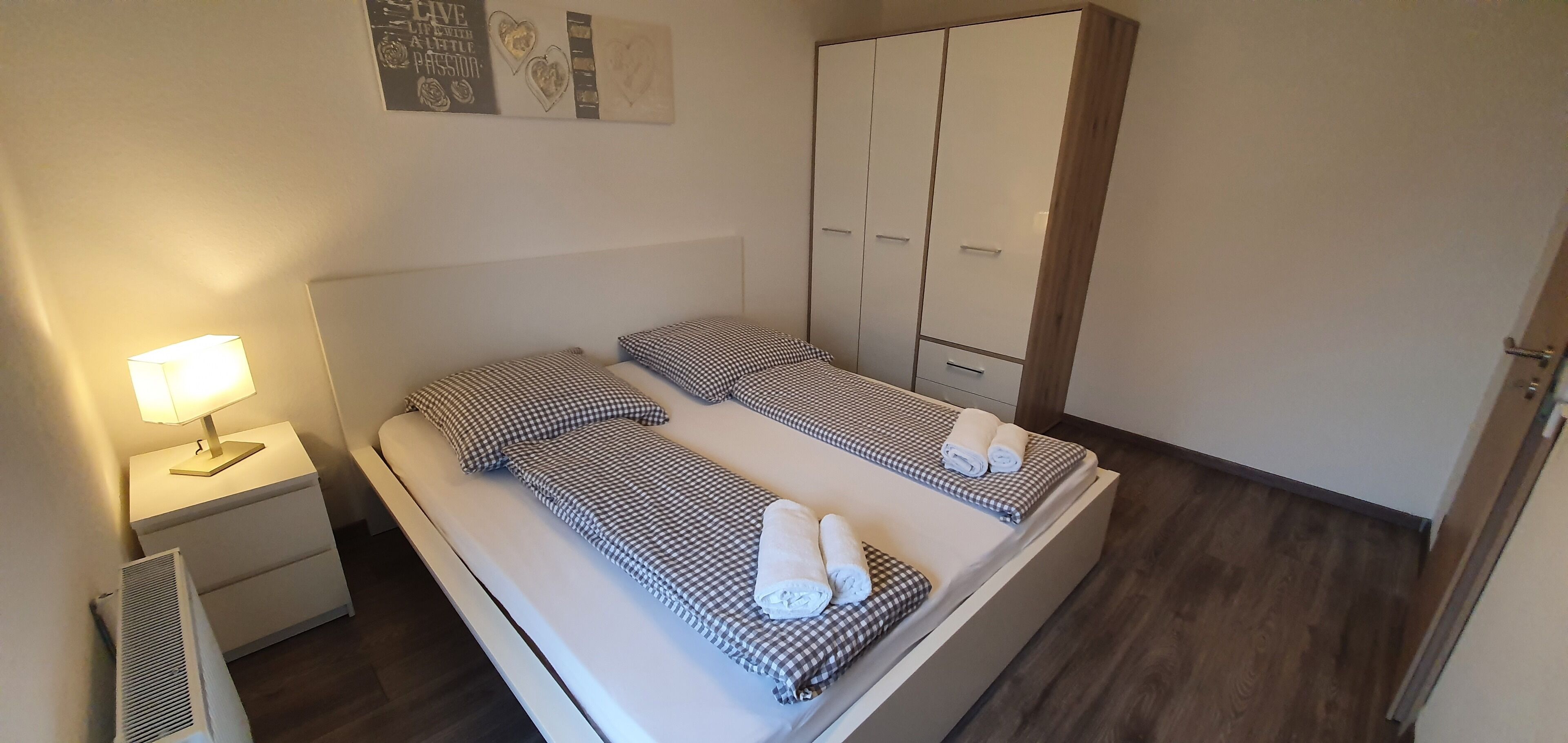 A small, neatly arranged bedroom with a single bed, a nightstand, a lamp, and a wardrobe.