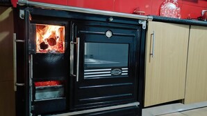 A black wood-burning stove with a glass door, a red wall, and wooden cabinets.