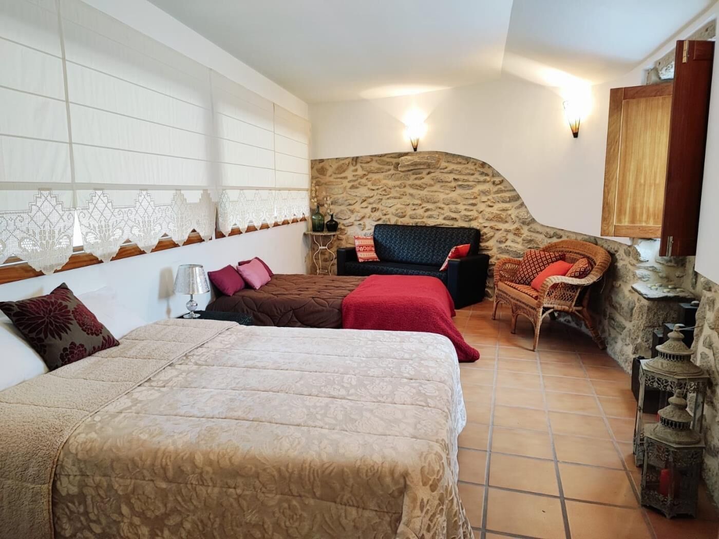 Un dormitorio con una cama grande, un sofá, una silla de mimbre y una pared de piedra.