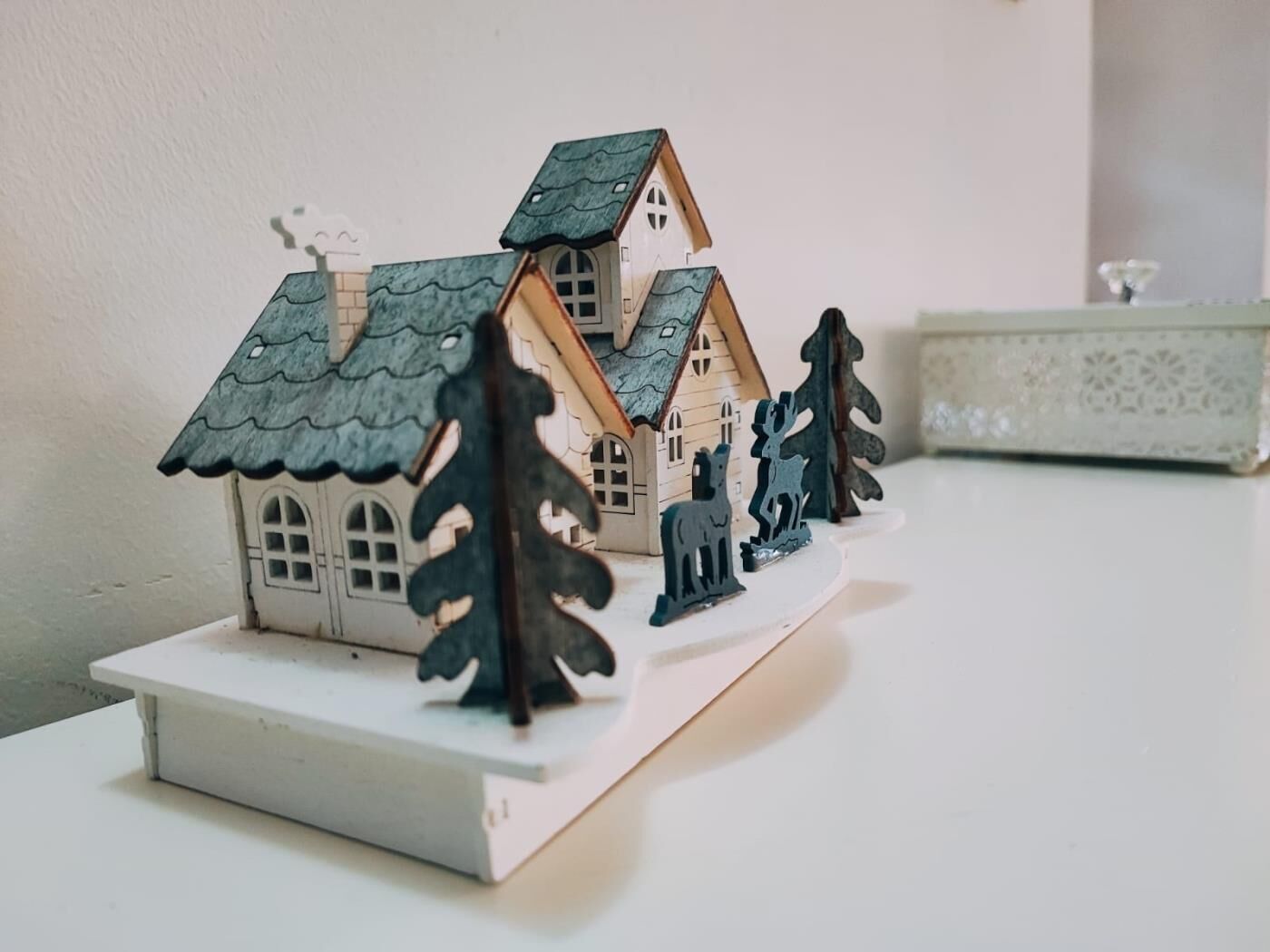 A model house with a peaked roof and multiple windows, accompanied by two tree figures.
