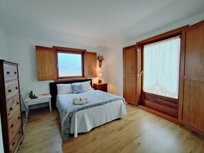 A bedroom with a bed, wooden wardrobe, a nightstand, a dresser, a window, and a view of the sea. - Casa da Telhada | Rustic | Rafting Capital | Northern Portugal (Melgaço)