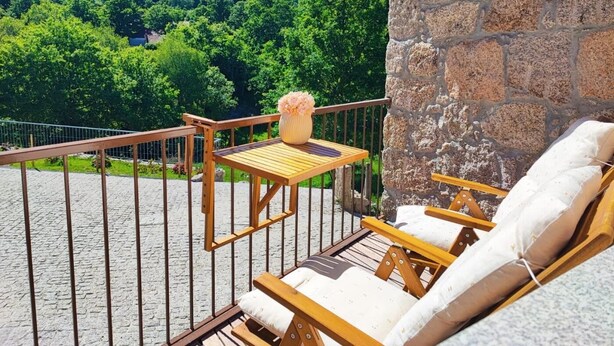 Un balcón con una pared de piedra, una mesa de madera con un florero y dos sillones de madera.