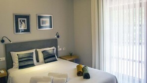 Un lit bien fait, avec du linge de lit blanc et deux oreillers, une table de chevet avec une lampe, et deux tableaux encadrés accrochés au mur.