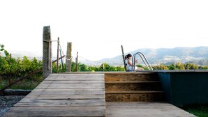 Une terrasse en bois mène à un escalier en pierre, d’où l’on peut admirer des vignobles et des montagnes en arrière-plan.