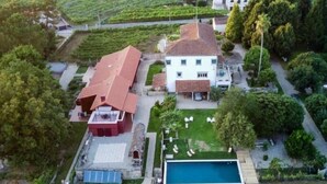 An aerial view of a property with a large house, a swimming pool, and well-maintained gardens.