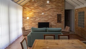 A cozy living room with a brick wall, a green sofa, a wooden dining table, and a TV mounted on the wall.