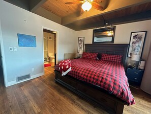 Cozy bedroom with a large bed, nightstand, and artwork-adorned walls.