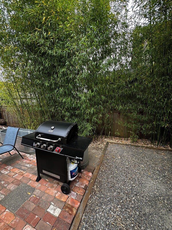 Un barbecue noir, avec un réservoir d’eau et une chaise en arrière-plan.