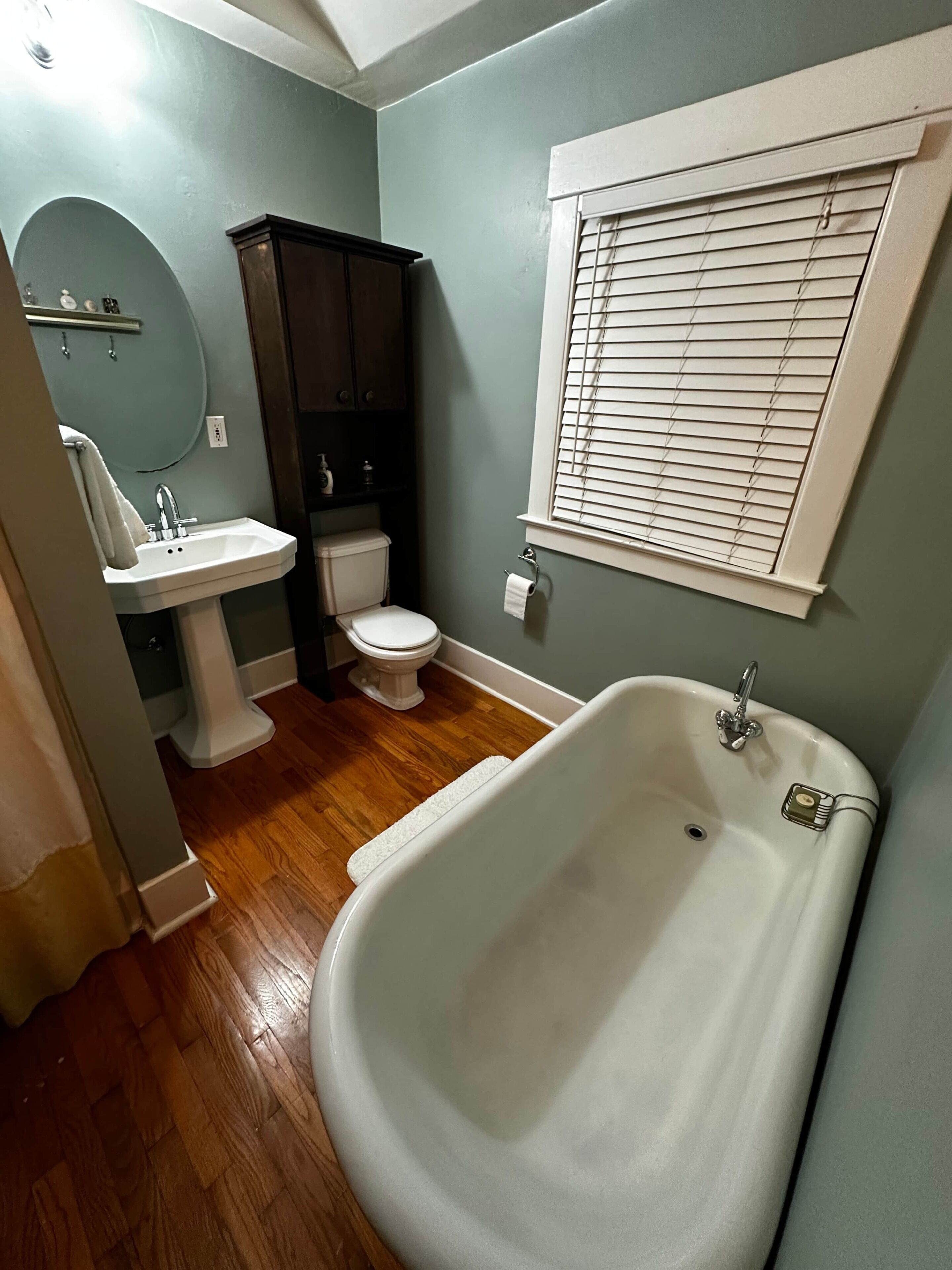 A bathroom with a bathtub, toilet, sink, and window with blinds.