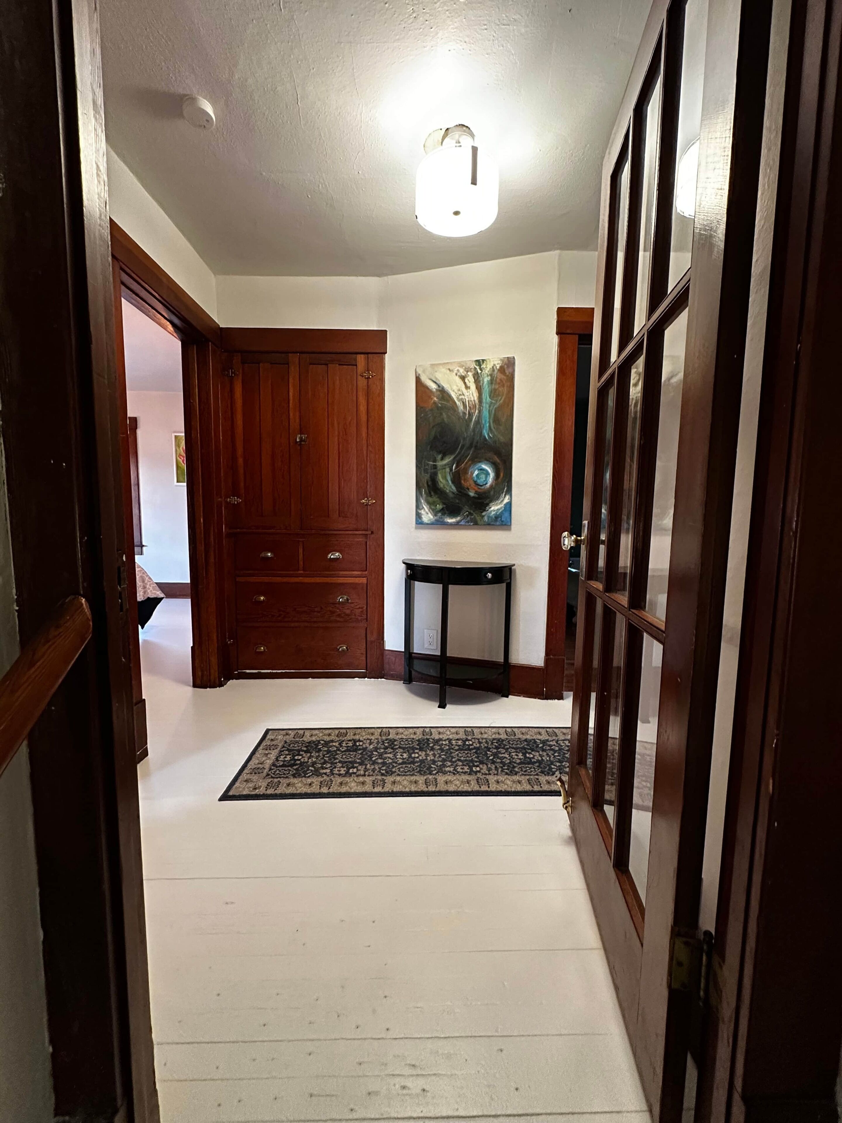 Un couloir avec une porte en bois, une table noire et un tableau accroché au mur.