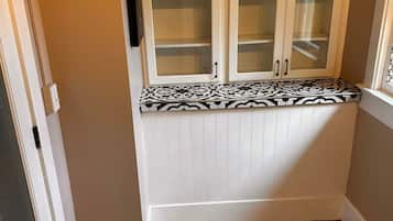 Een hoek met een ingebouwde bank, een witte kast met glazen deuren en een betegelde vloer.