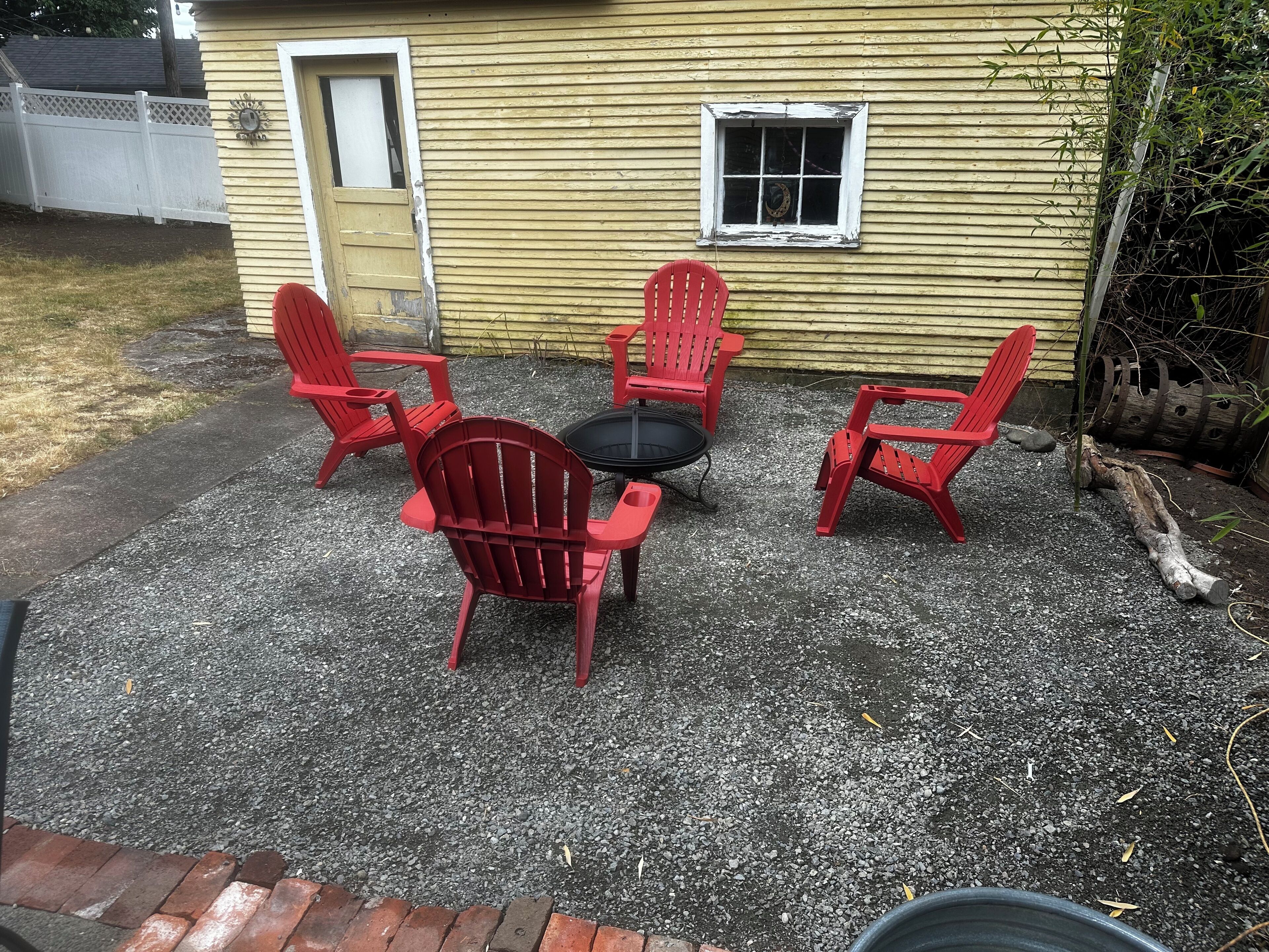 A patio area with four red Adirondack chairs and a small round table.