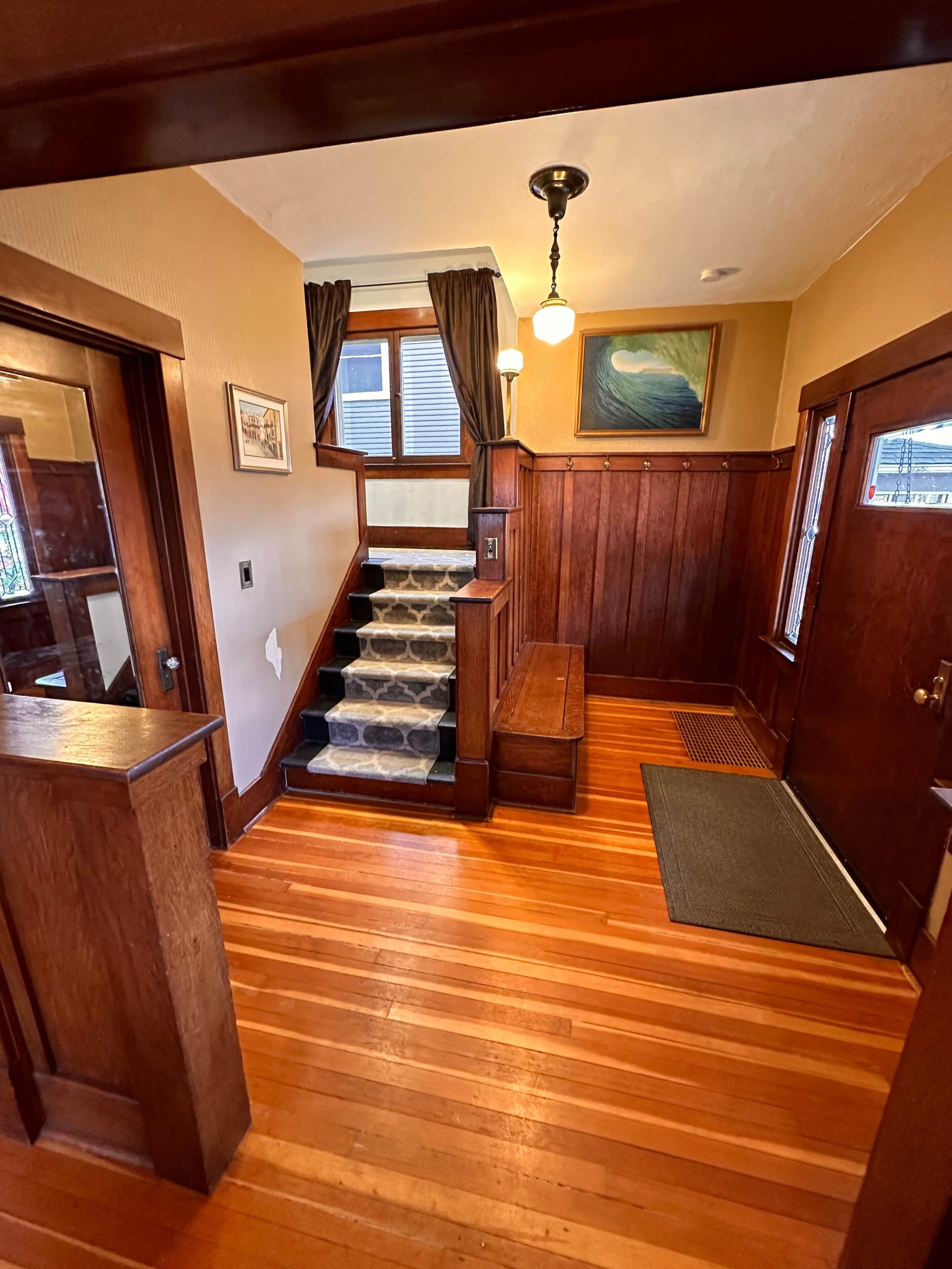 A wooden staircase with a stone tread, leading to a landing with a bench and a rug.