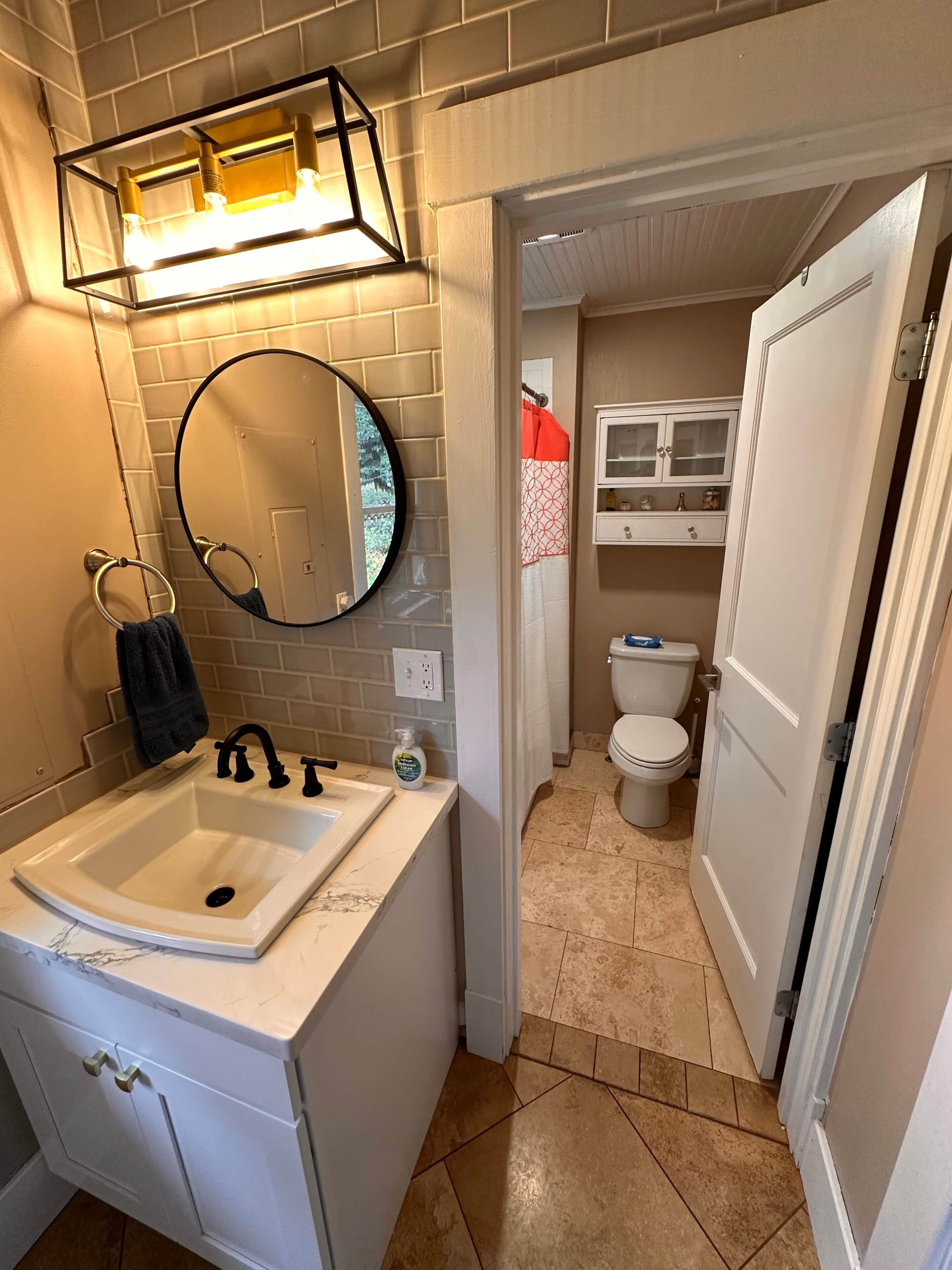 A bathroom with a white sink, a round mirror, a towel ring, and a light fixture above the mirror.