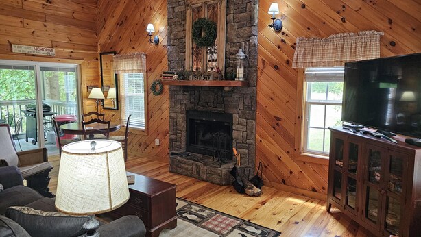 A cozy cabin interior with a stone fireplace, wooden walls, a television, and a dining area. - Cardinal Nest -Mountain views, babbling stream, fields to play in, privacy! (Blairsville)