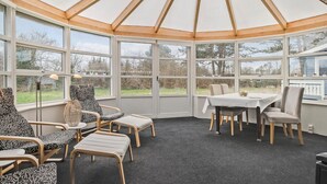 Een wintertuin met houten plafond, grote ramen en een gedekte eettafel voor vier personen.
