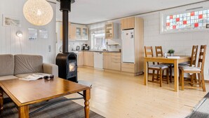 Een moderne keuken met een houtkachel, een eethoek met een houten tafel en stoelen, en een woonkamer met een bank en salontafel.