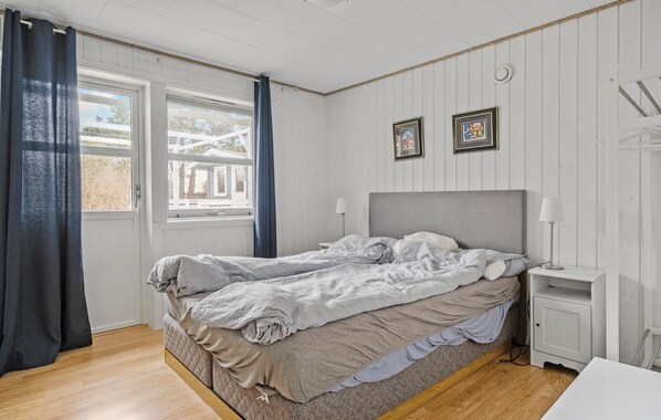 A bedroom with a bed, a nightstand, a lamp, and a window with curtains.