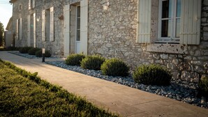 A stone building with white shutters and a concrete pathway.