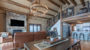 A spacious living area with a stone fireplace, a large flat-screen TV, leather sofas, and a wooden dining table. - Gorgeous Alpine Hollow on 3 acres - Hot Tub (Alpine)