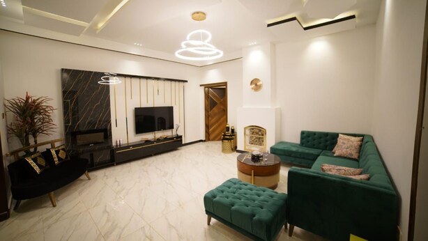 Una sala de estar moderna con un sofá negro, sillones verdes, piso de mármol y un televisor.