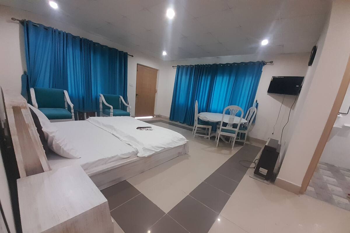 A hotel room with a bed, two chairs, a small table, a TV, and a door.