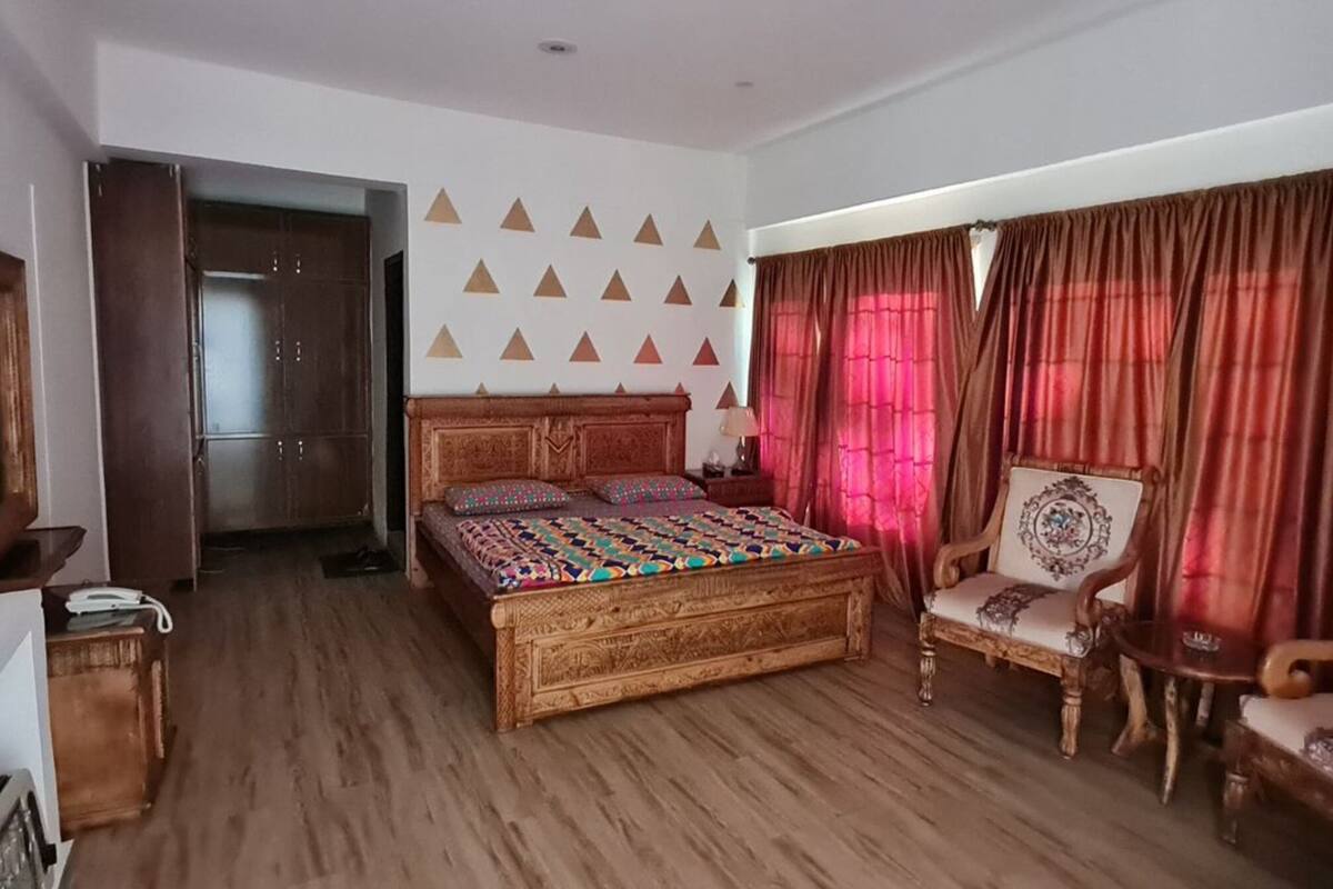 A bedroom with a wooden bed, two chairs, a wardrobe, and a mirror on the wall.