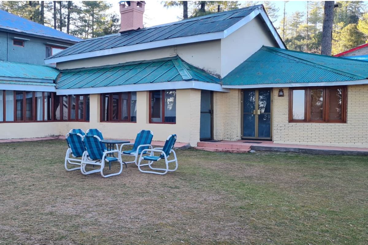 A building with a green roof, multiple windows, and a small lawn with a table and chairs.