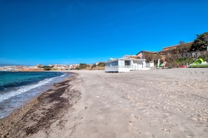 A beach with a white building, clear blue sky, and calm sea.
