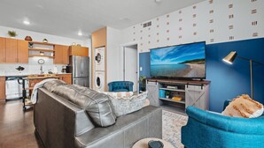 A modern living room with a grey sofa, a blue armchair, and a flat-screen TV. - *NEW* Great Escape 404 2BR Condo Near Downtown and Bay (Traverse City)