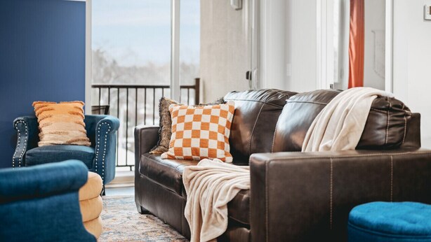A living room with a leather sofa, a blue armchair, and a patterned throw blanket. - *NEW* Great Escape 404 2BR Condo Near Downtown and Bay (Traverse City)