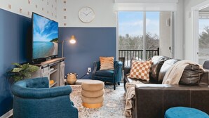 Una sala de estar moderna con un televisor de pantalla plana grande, un sillón azul, un sofá de cuero marrón y una alfombra estampada.