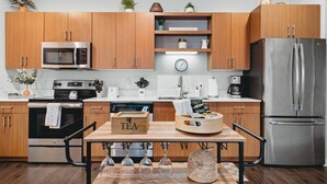 Una cocina moderna con armarios de madera, electrodomésticos de acero inoxidable, una cafetera y una caja de té en la encimera.