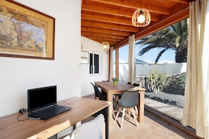 A wooden dining table with chairs, a laptop, a framed map, and a view of a palm tree and cactus through large windows.