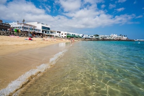 A beach with clear water, a sandy shore, and buildings in the background. - Vacation Villa 'La Rinconera' with Private Terrace, Private Garden and Wi-Fi (Playa Blanca)