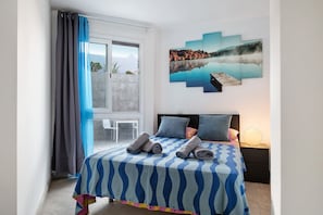 A bedroom with a bed, a nightstand, a window with curtains, and a wall-mounted artwork.