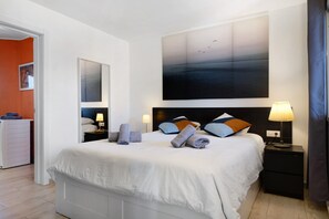 Habitación de hotel moderna con una cama grande, una mesita de noche con lámpara, una obra de arte en la pared y vistas al pasillo.
