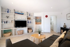 A modern living room with a flat-screen TV, wooden shelves, a sofa, and a dining table.