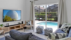 A modern living room with a large flat-screen TV, comfortable seating, a pool view, and a glass door leading outside. - Super Spacious House w/ Private Pool and Game Room (Kissimmee)