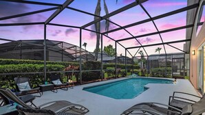 A pool area with a glass enclosure, lounge chairs, and a view of the surrounding landscape. - Super Spacious House w/ Private Pool and Game Room (Kissimmee)