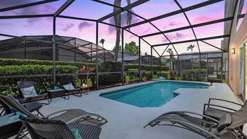A pool area with a glass enclosure, lounge chairs, and a view of the surrounding landscape.