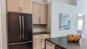 A modern kitchen with wooden cabinets, a stainless steel refrigerator, a black countertop, and a fruit basket. - Super Spacious House w/ Private Pool and Game Room (Kissimmee)