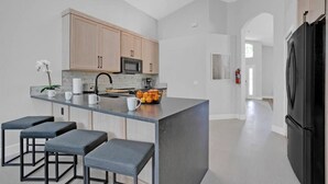A modern kitchen with a central island, bar stools, a microwave, and a refrigerator. - Super Spacious House w/ Private Pool and Game Room (Kissimmee)