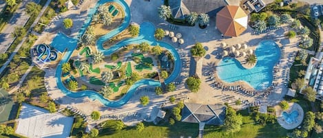An aerial view of a resort with multiple swimming pools, a golf course, and a large parking area.