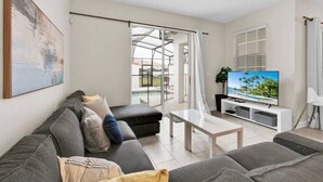 A modern living room with a grey sofa, a coffee table, and a TV on a white stand. - Spacious Home,Private Pool-September Special Price (Kissimmee)